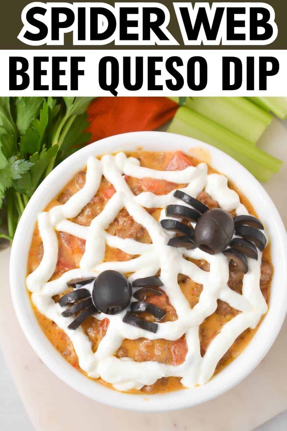 A bowl of beef queso dip topped with sour cream in a spider web design and black olives shaped like spiders, surrounded by celery and parsley.