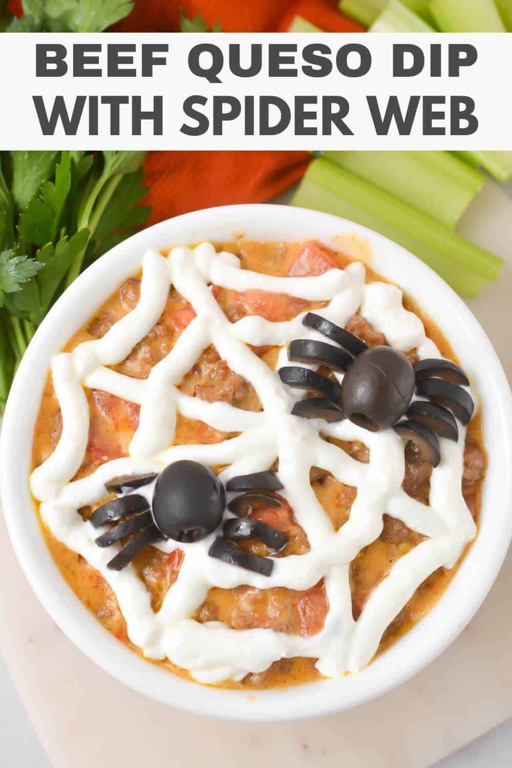Bowl of beef queso dip with a sour cream spider web and black olive spiders, garnished with celery and parsley.