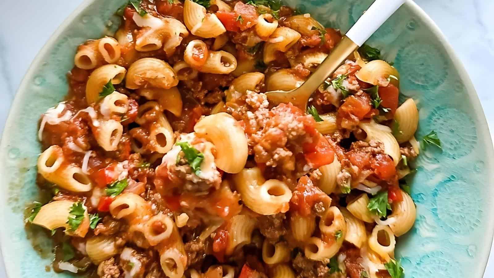 A bowl of pasta with ground meat, tomato sauce, and herbs, with a fork resting inside.