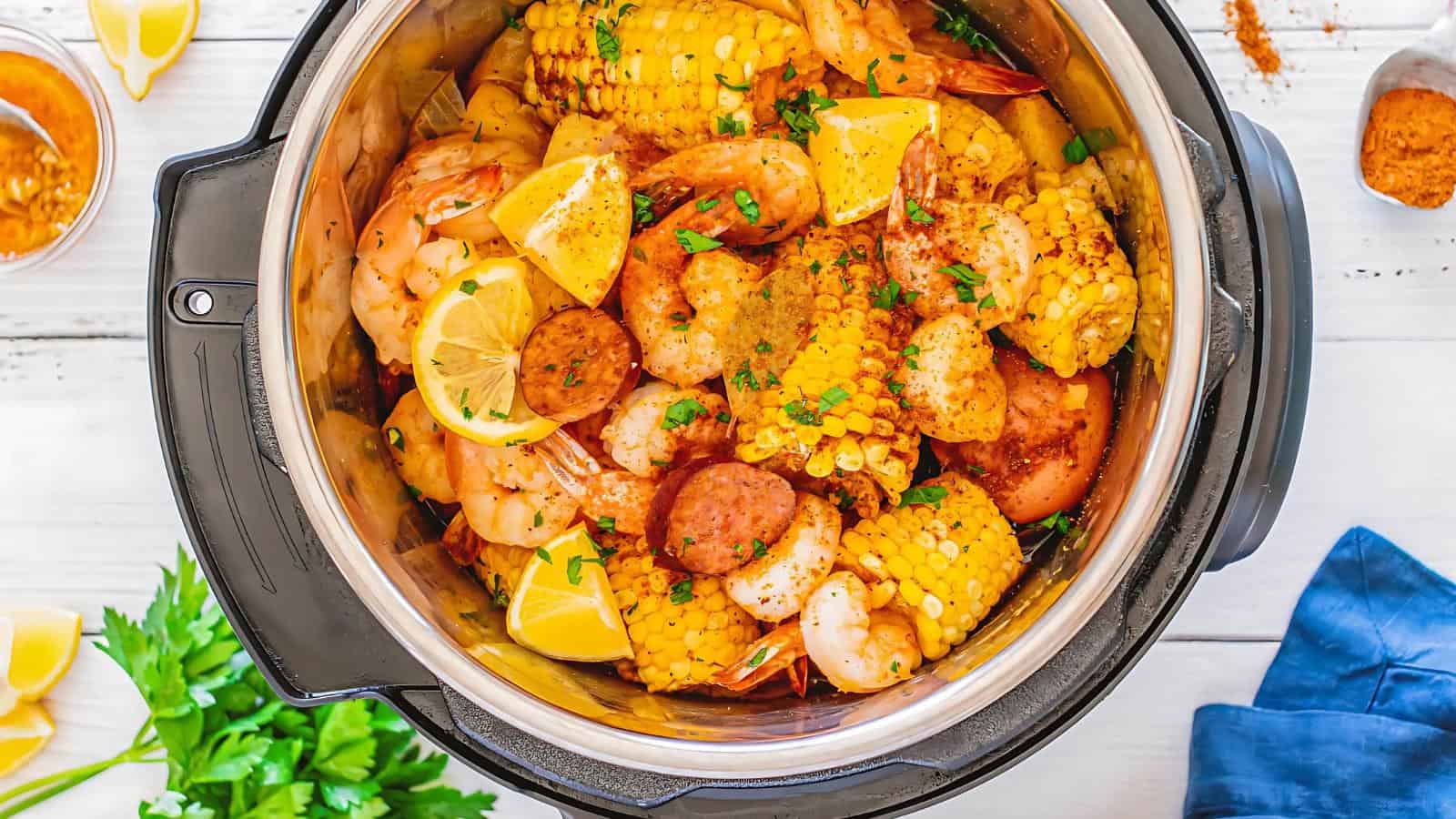 An Instant Pot filled with shrimp, corn, sausage slices, potatoes, and lemon wedges, garnished with herbs.