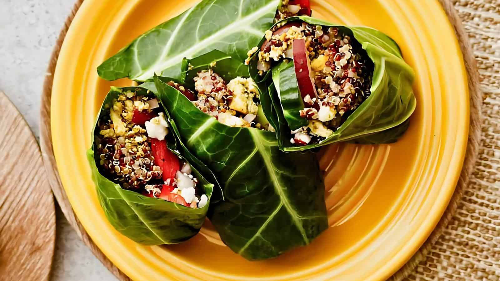 Three collard green wraps filled with quinoa, red bell peppers, and feta cheese on a yellow plate.