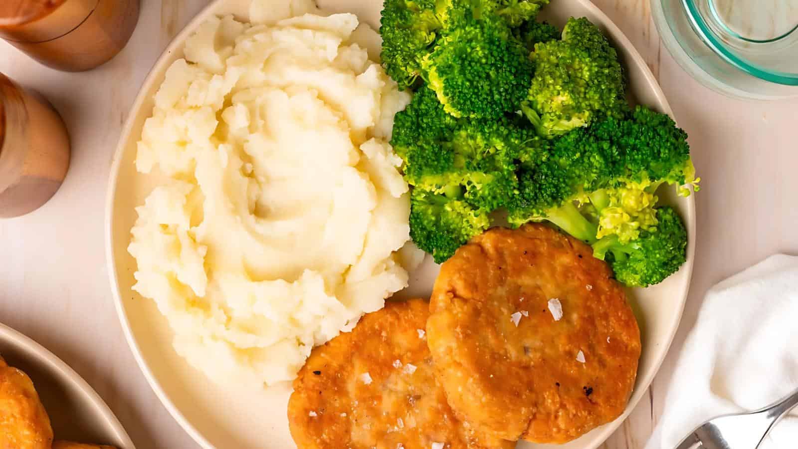 A plate with mashed potatoes, broccoli, and two breaded chicken patties.