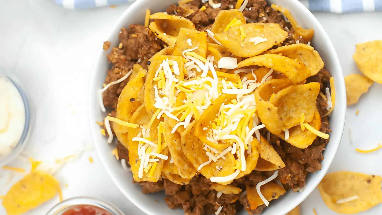 A bowl of Frito pie with ground beef, topped with corn chips and shredded cheese.
