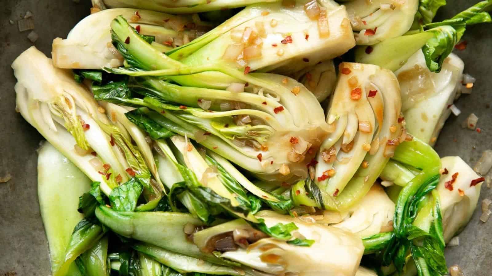 Sliced and sautéed bok choy sprinkled with red pepper flakes and chopped garlic on a plate.