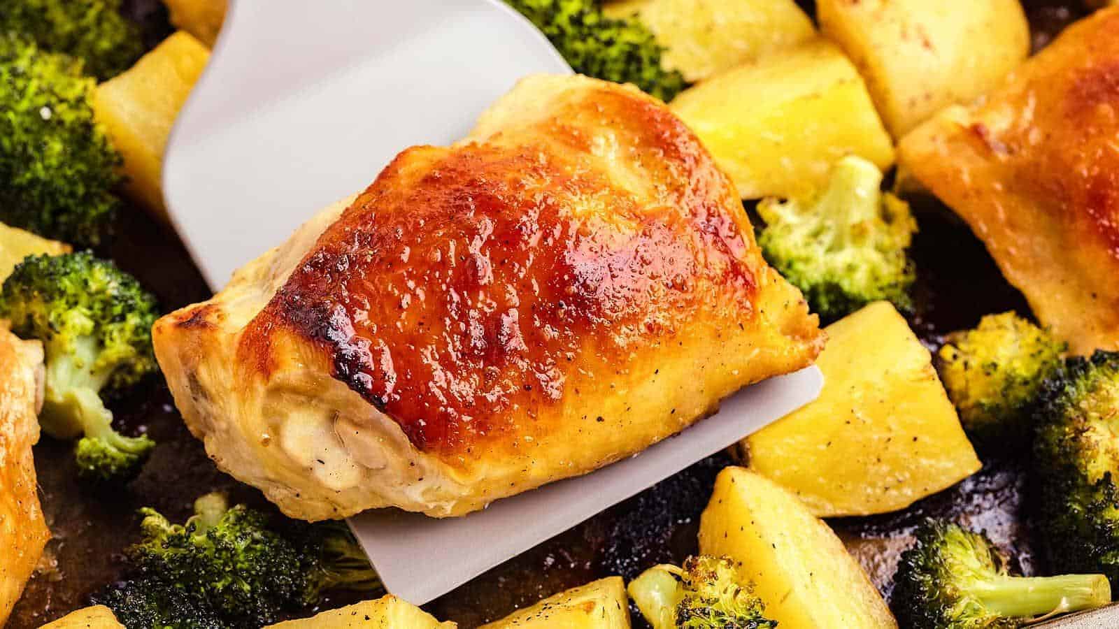 Close-up of cooked chicken pieces on a spatula, surrounded by roasted potatoes and broccoli.