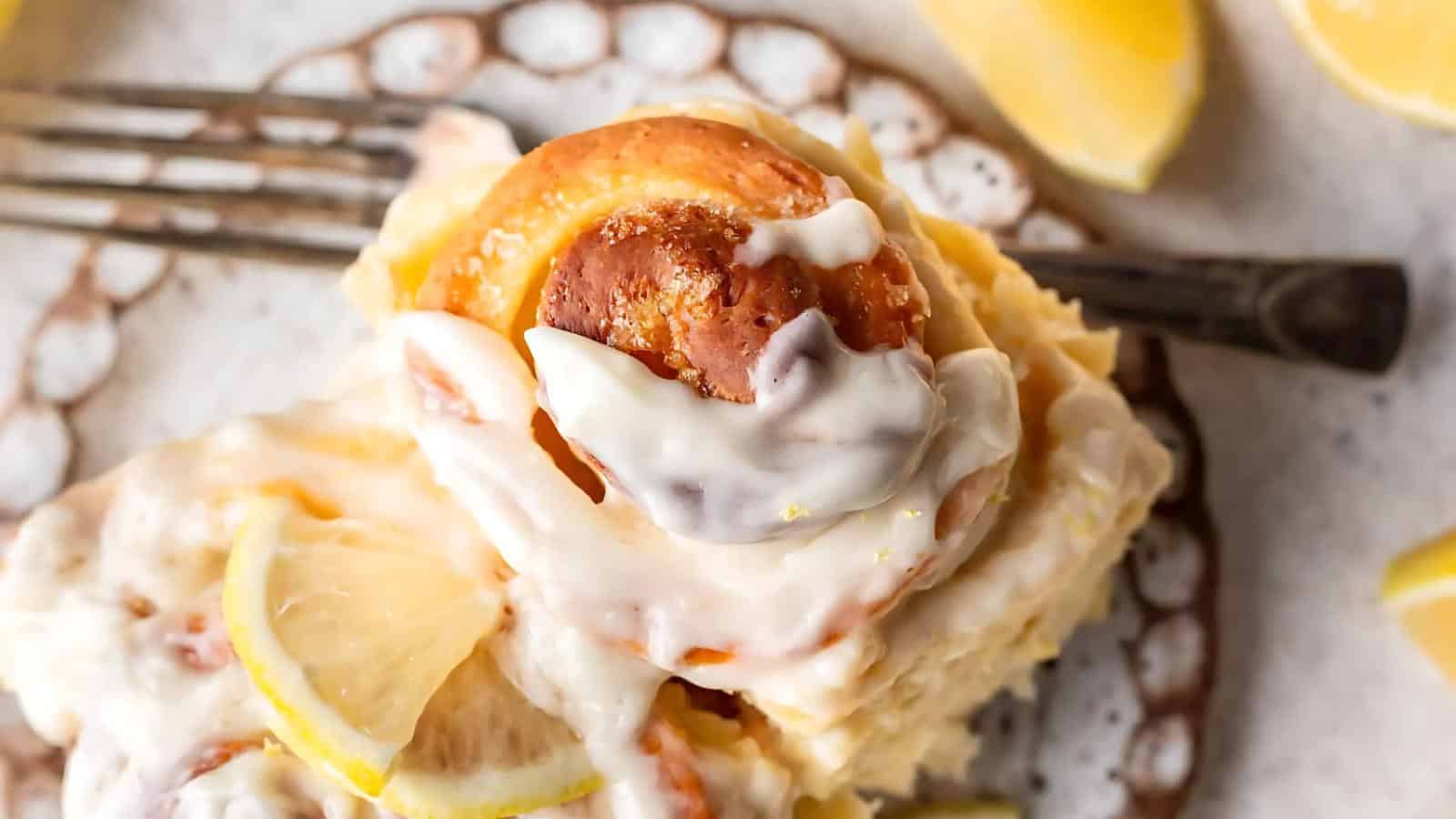 Close-up of a glazed lemon cinnamon roll on a plate with a fork, garnished with lemon slices.