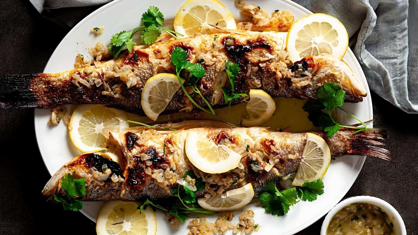 Two grilled fish on a plate garnished with lemon slices, herbs, and chopped onions.