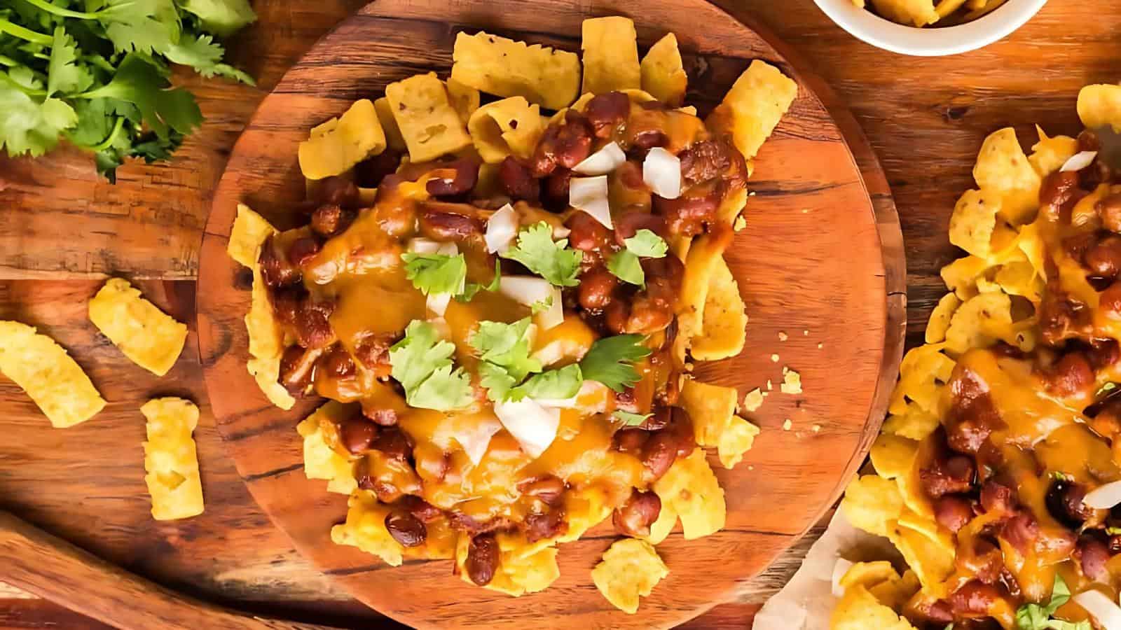 A wooden plate of nachos topped with melted cheese, beans, chopped onions, and cilantro.