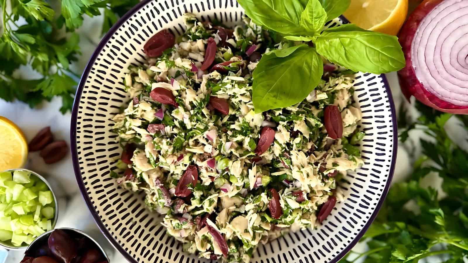 A bowl of tabbouleh salad with fresh greens, almonds, and olives, garnished with basil leaves.