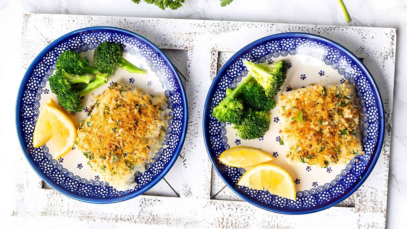 Two blue and white plates with breaded chicken, broccoli florets, and lemon wedges, arranged on a white tray.