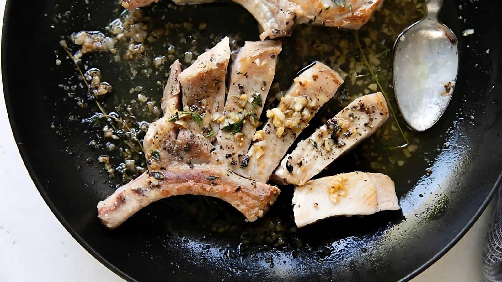 Cooked pork chops seasoned with herbs and garlic in a pan, alongside a spoon.