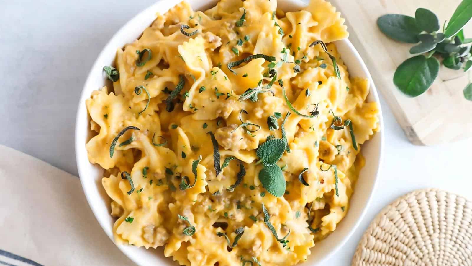 A bowl of bowtie pasta with creamy cheese sauce, topped with herbs and garnished with fresh sage leaves.