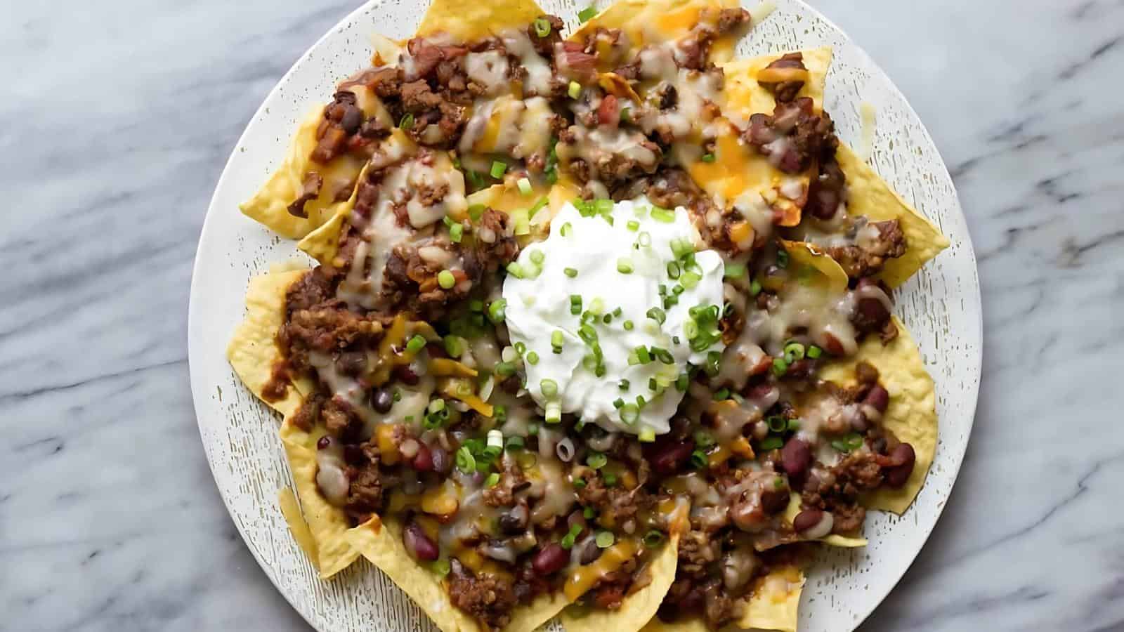 Plate of nachos topped with melted cheese, seasoned ground meat, beans, diced vegetables, sour cream, and chopped green onions.