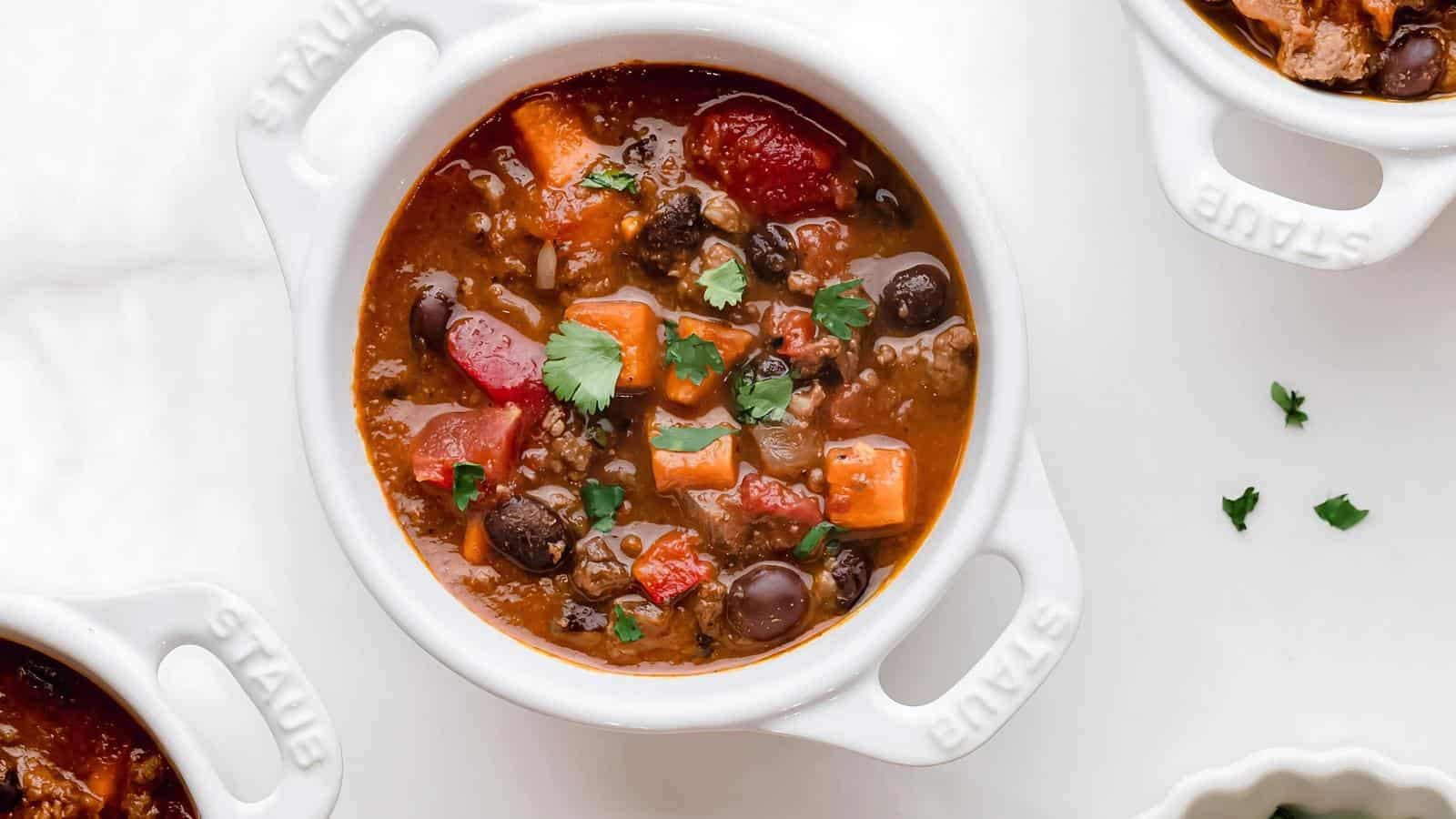 White bowls filled with chili, featuring beans, tomatoes, meat, and garnished with cilantro.