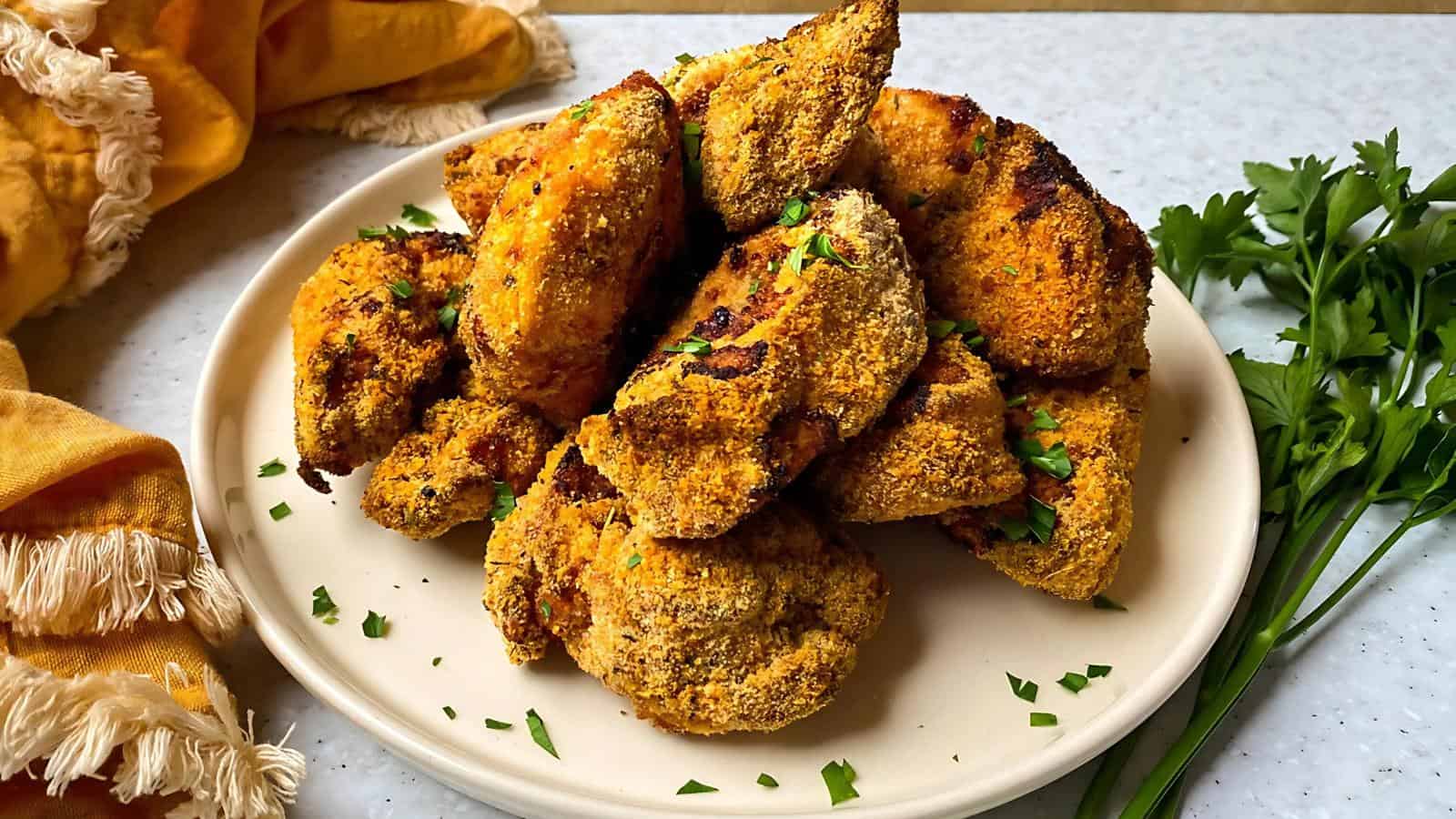 A plate of breaded, crispy cauliflower wings garnished with chopped parsley. A yellow cloth and sprigs of parsley are beside the plate.