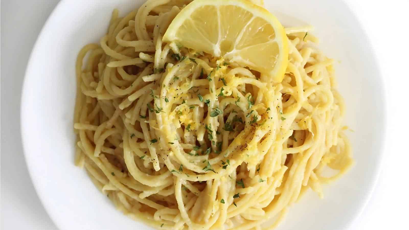 A plate of spaghetti topped with a lemon slice, garnished with herbs.