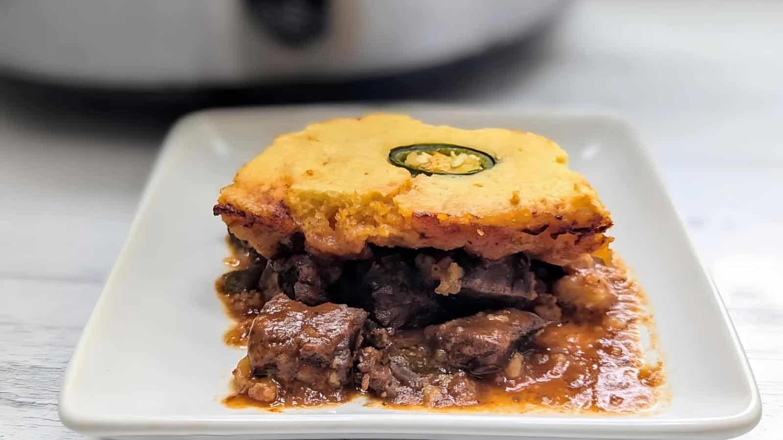 A plate of beef pot pie topped with cornbread and garnished with a slice of jalapeño.