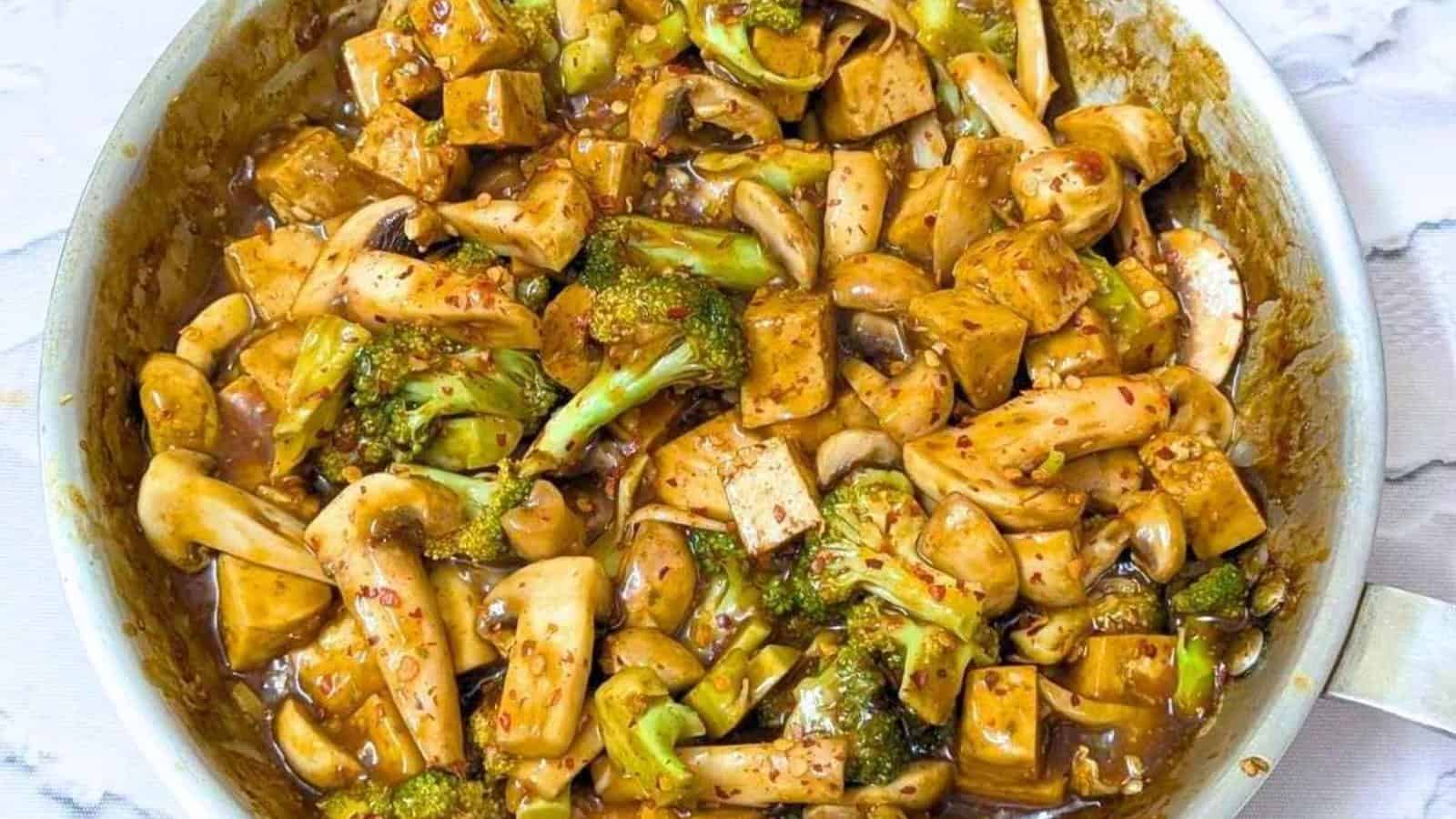 Stir-fried vegetables and tofu in a savory sauce, featuring broccoli and mushrooms, in a round skillet.