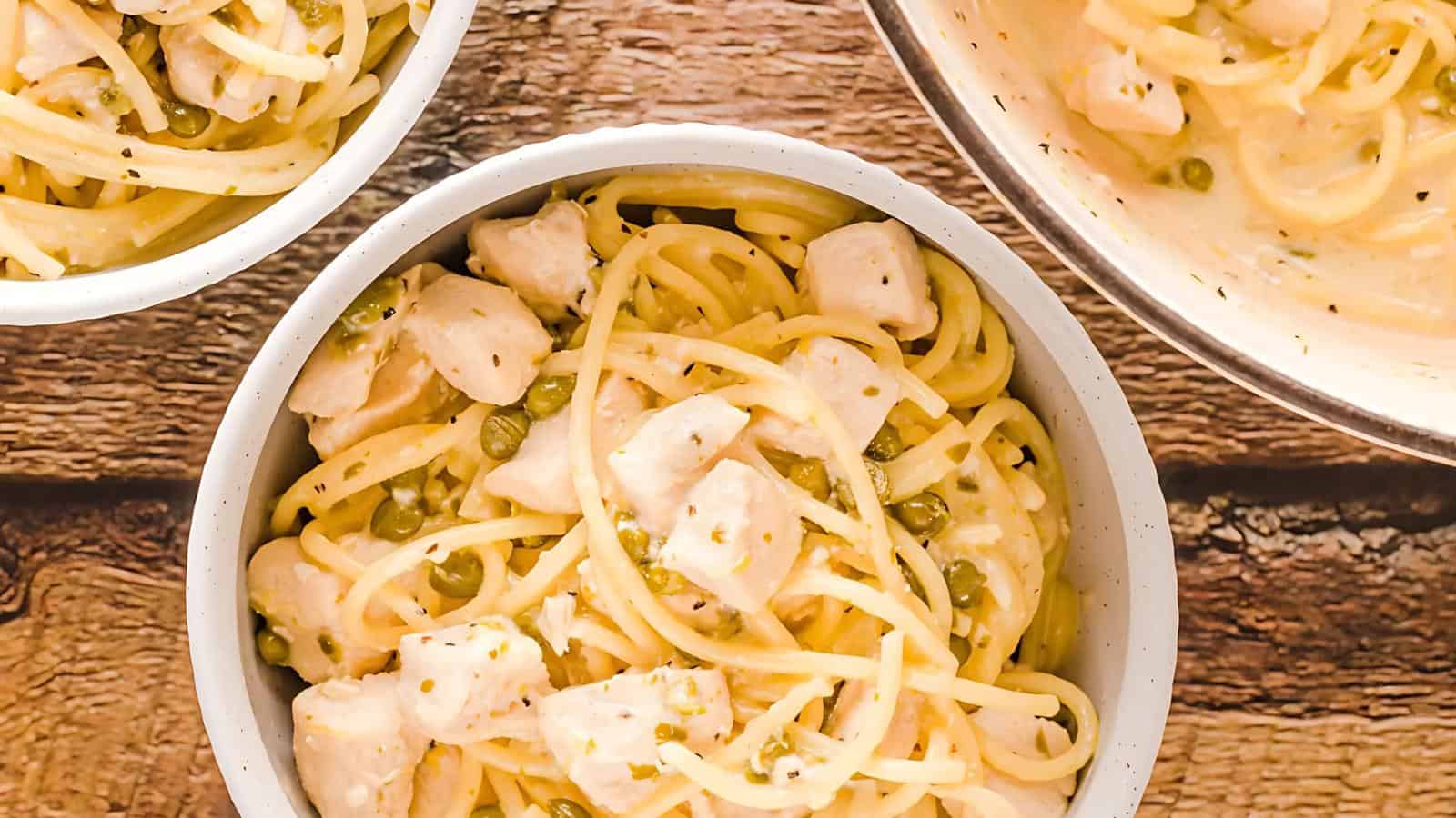 Bowls of pasta with chicken pieces and green peas, served in a creamy sauce on a wooden table.