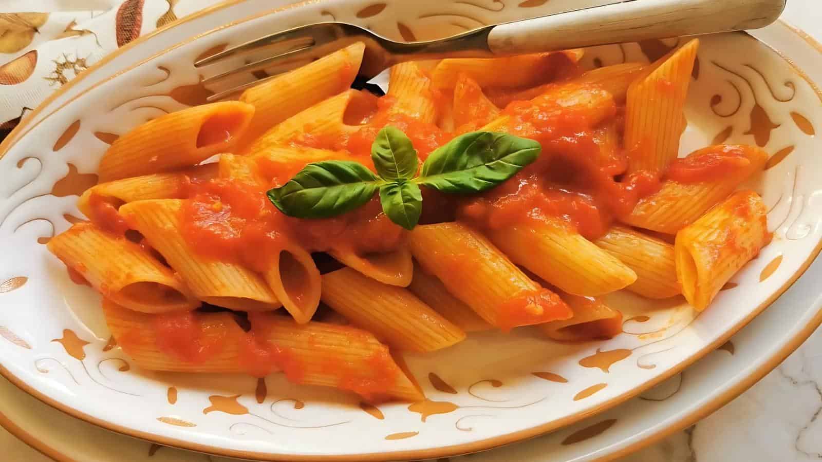 A plate of penne pasta with tomato sauce, garnished with fresh basil, and a fork on the side.