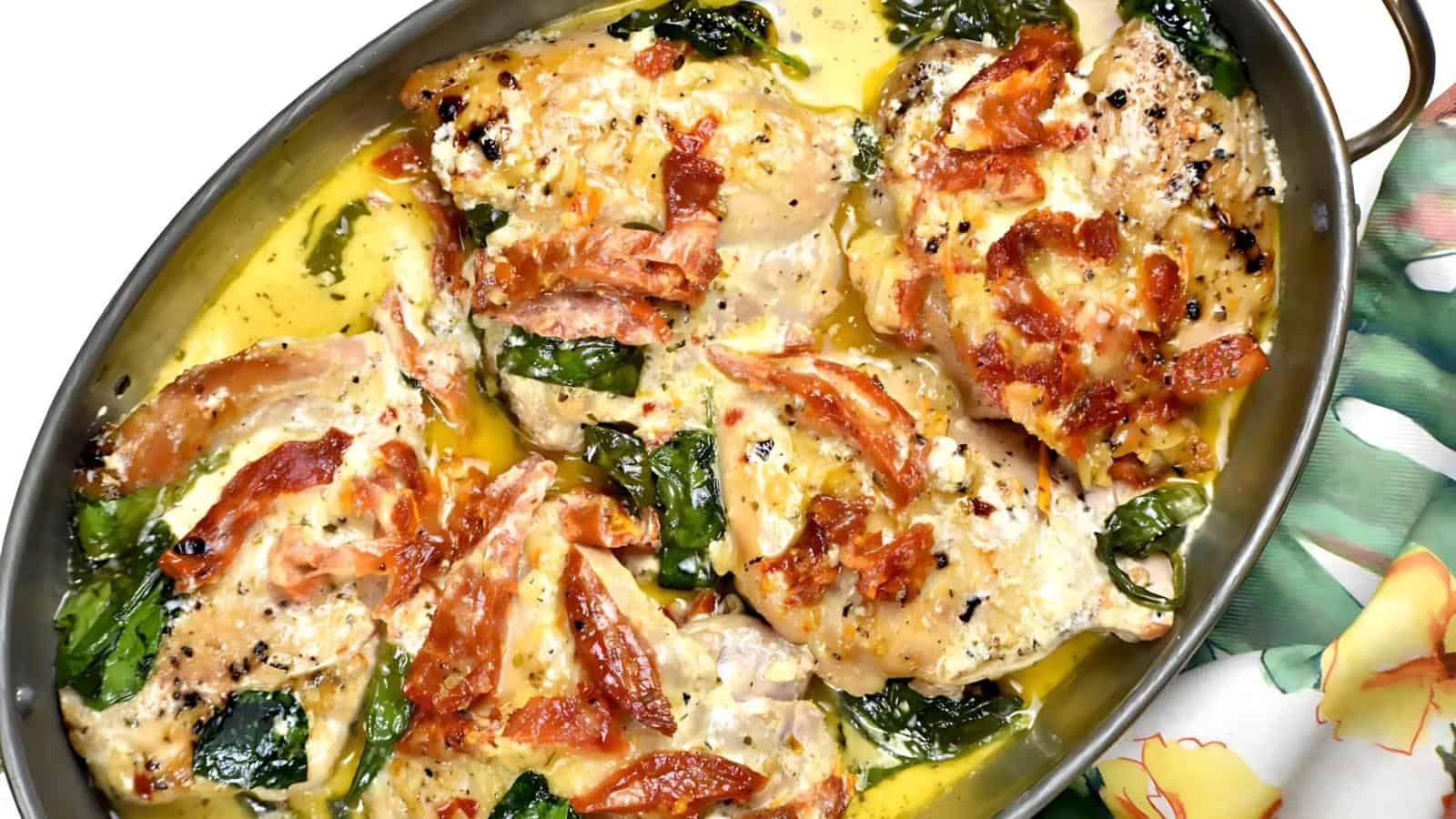 Baked chicken breasts with spinach, bacon, and creamy sauce in an oval dish.