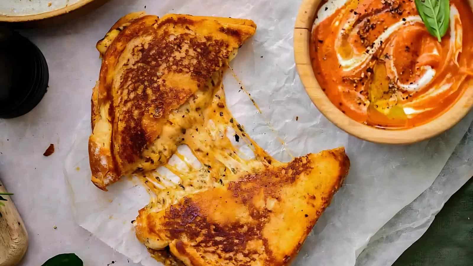 Grilled cheese sandwich on parchment paper, with melted cheese oozing out. A bowl of orange and white swirled dipping sauce is beside it.
