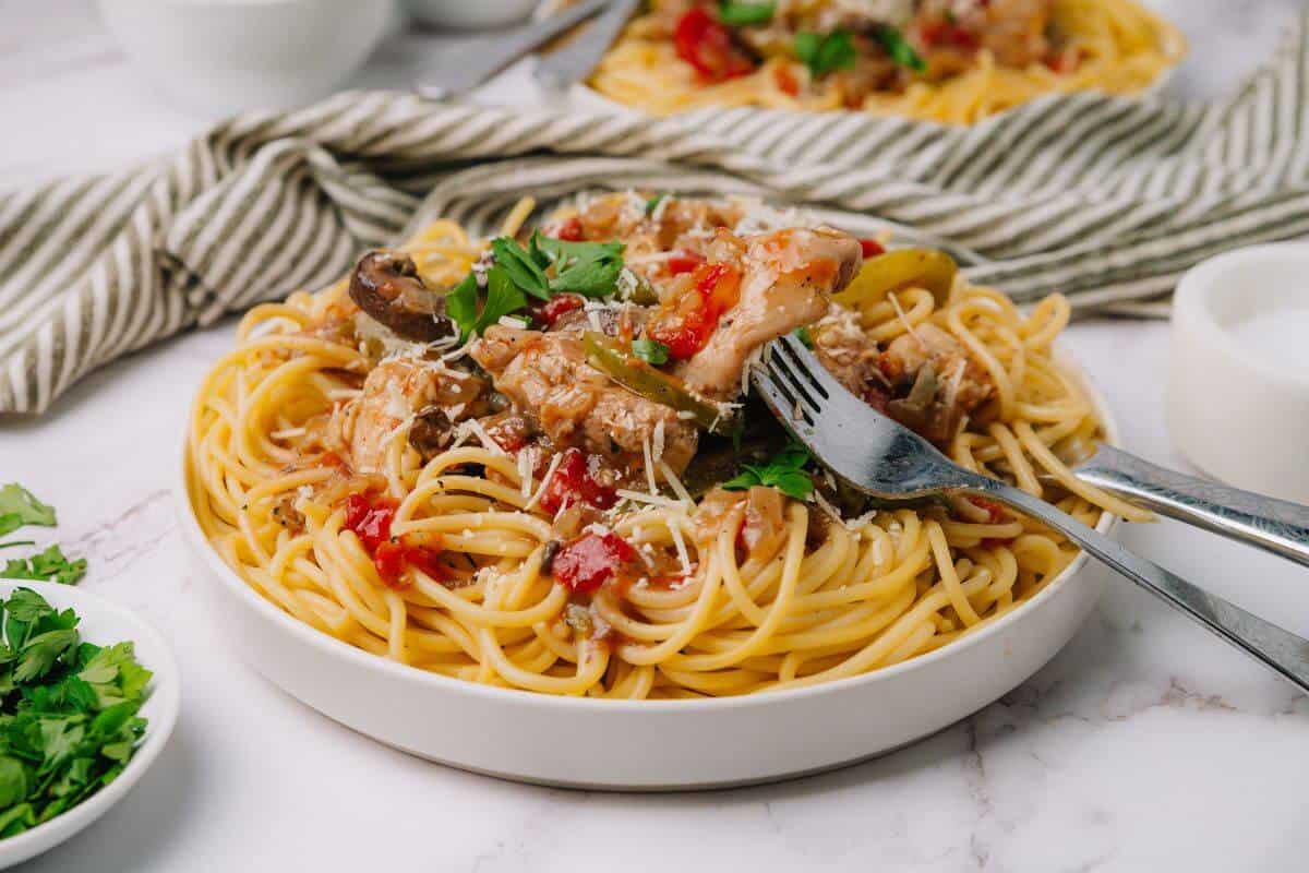 Plate of spaghetti topped with mushrooms, tomatoes, and herbs, garnished with grated cheese. Fork resting on the plate.