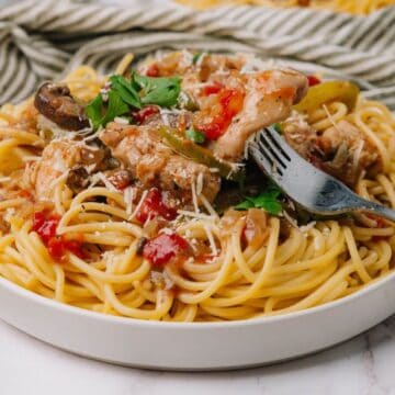 Plate of spaghetti topped with tomato sauce, mushrooms, and herbs, with a fork and spoon on the side.