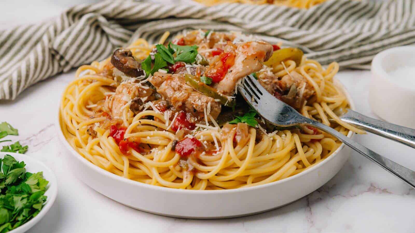 Plate of spaghetti topped with tomato sauce, mushrooms, and herbs, with a fork and spoon on the side.