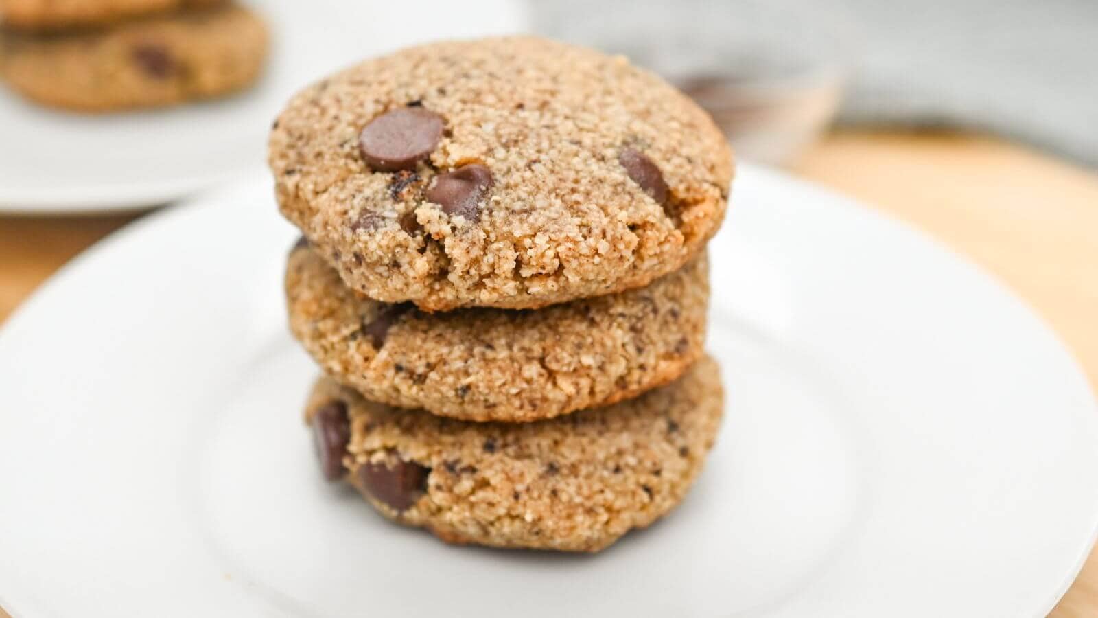Three chocolate chip cookies stacked on a white plate.
