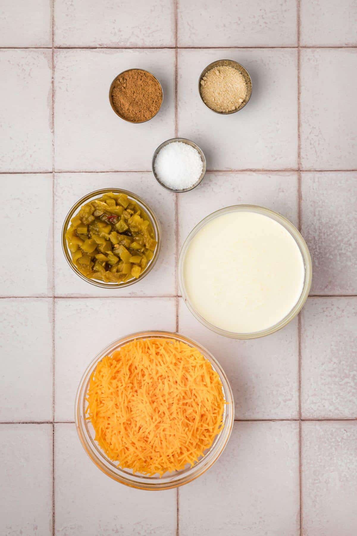 Ingredients on a tiled surface: grated cheese, chopped green chilies, flour, salt, and two small bowls of spices.