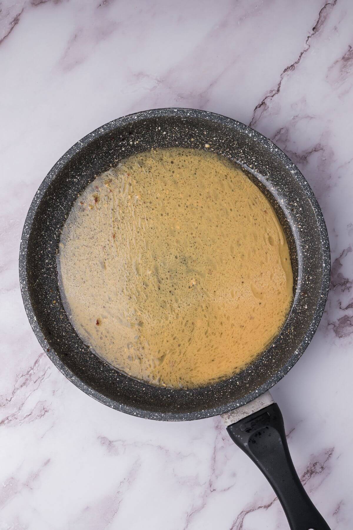 A non-stick frying pan on a marbled surface with a light brown liquid content.