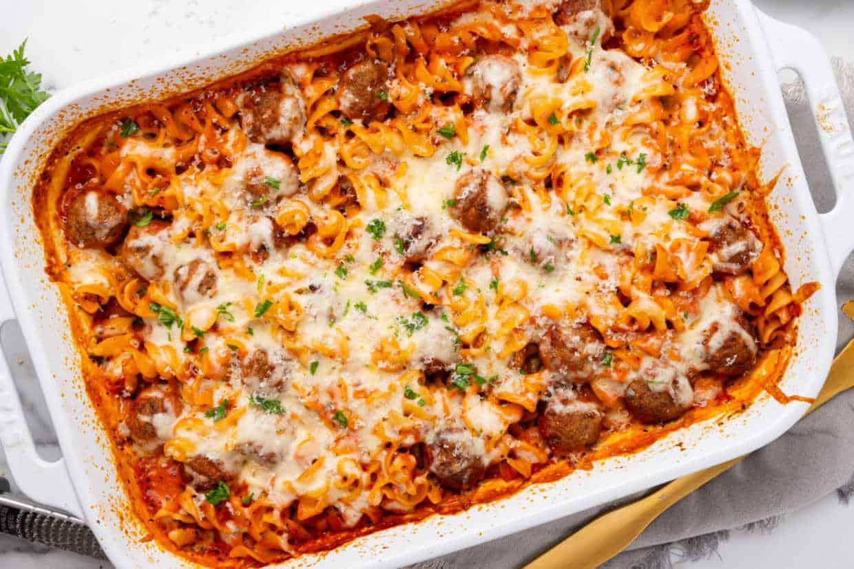 Baked pasta with meatballs and melted cheese in a white casserole dish.