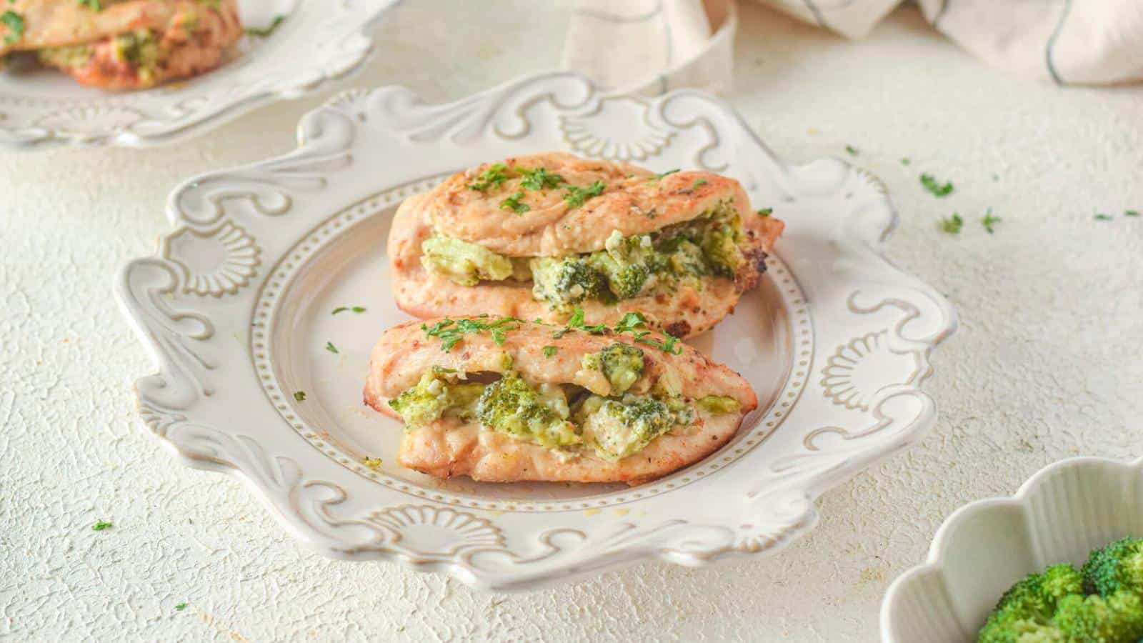 Two pieces of chicken stuffed with broccoli and cheese on an ornate white plate, garnished with chopped herbs.