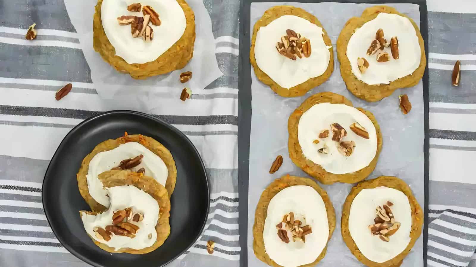 Cookies with white icing and pecan pieces on a black plate and a grid-patterned cloth.