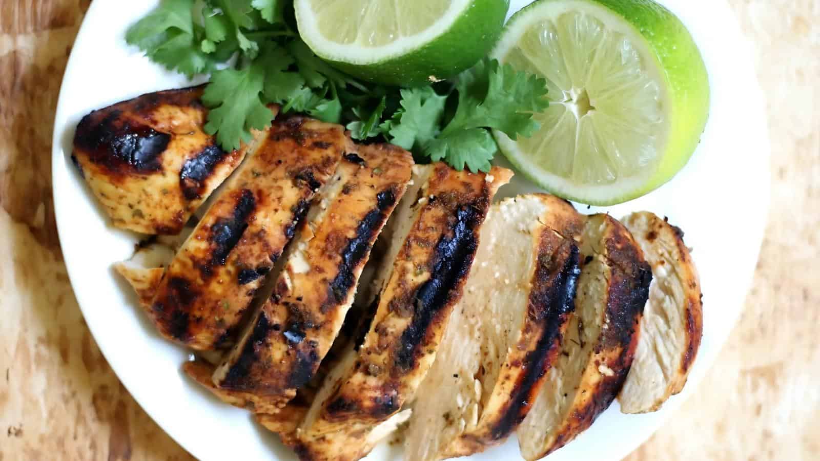 Sliced grilled chicken breast on a white plate with lime slices and cilantro garnish.