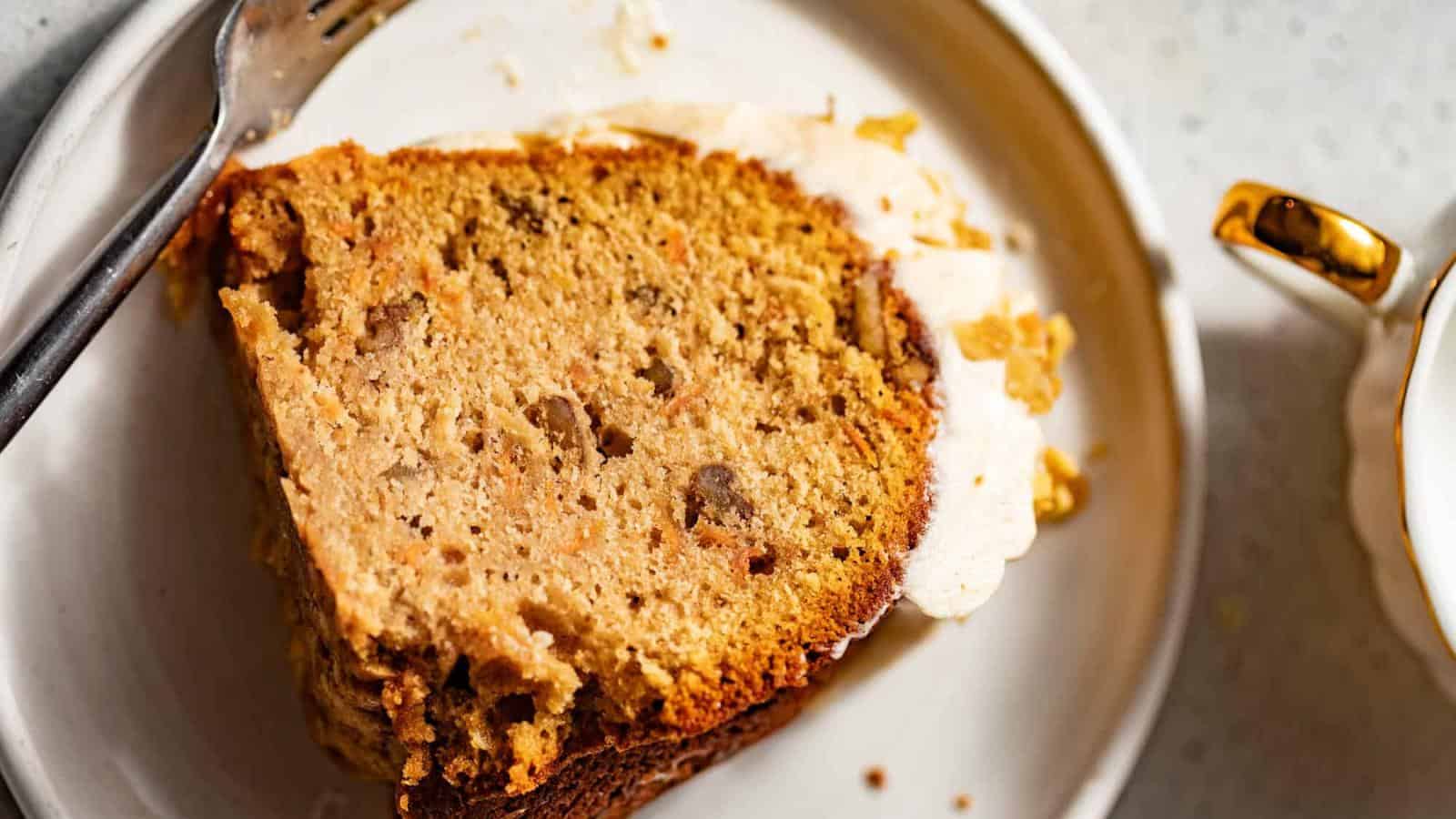 A slice of brown bread with visible nuts on a white plate, accompanied by a fork.