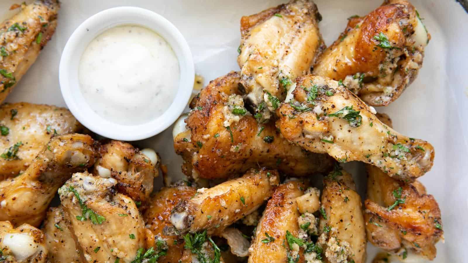 A plate of seasoned chicken wings garnished with herbs, served with a small bowl of dipping sauce.