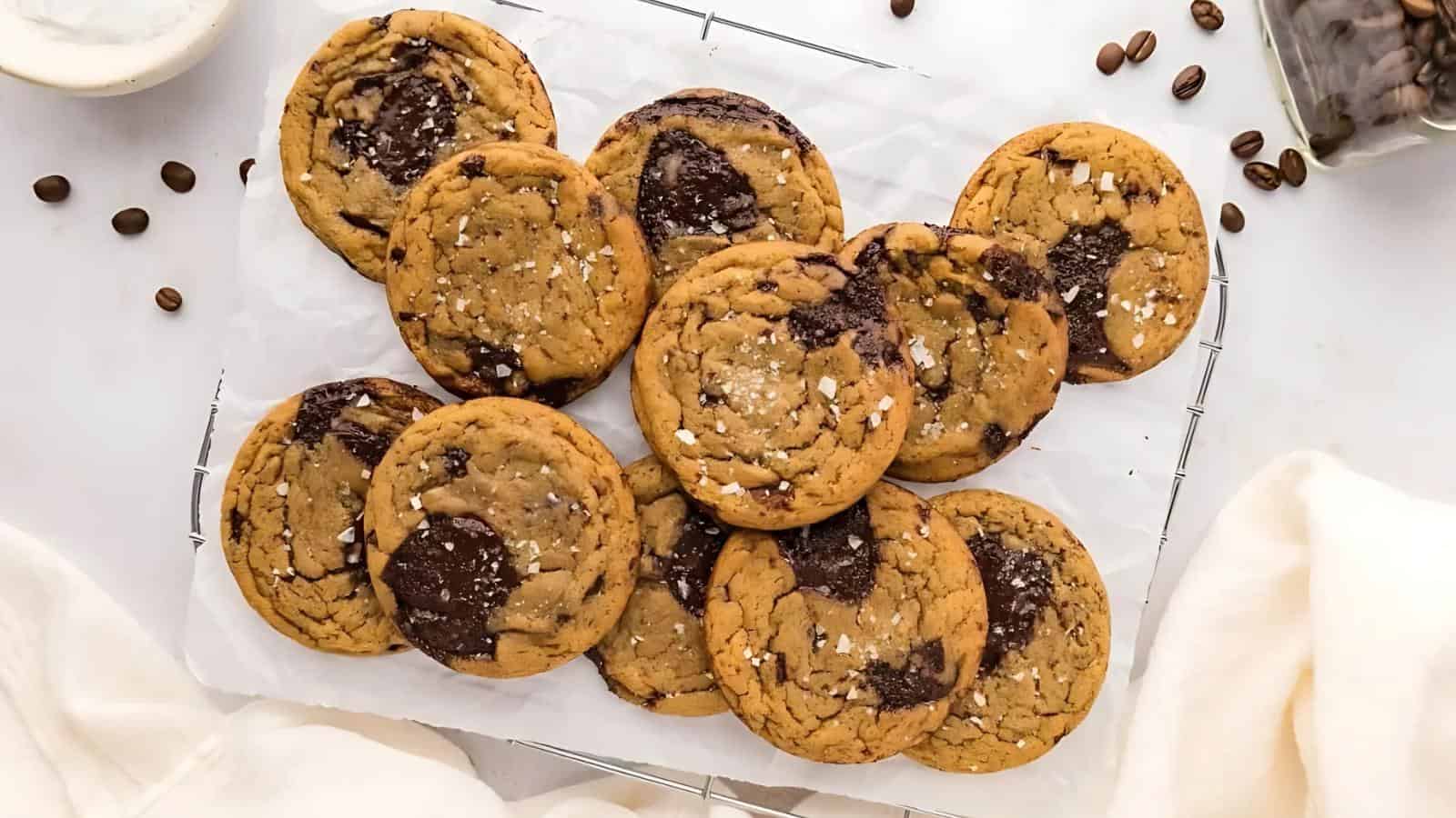 A cooling rack holds ten chocolate chip cookies with visible chocolate chunks and a sprinkle of sea salt on top.
