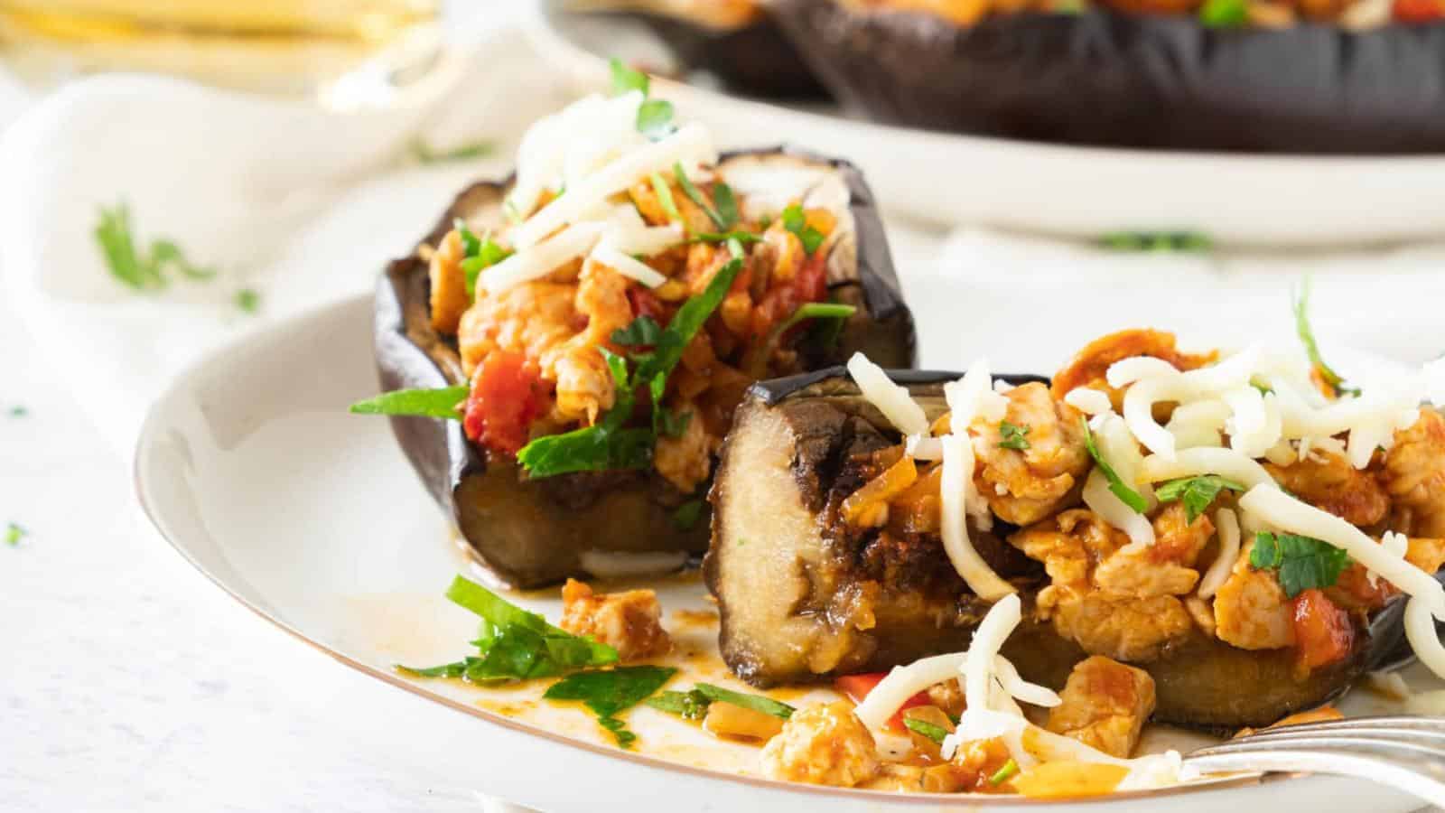 Two roasted eggplant halves filled with a vegetable and cheese mixture, garnished with fresh herbs, on a white plate.