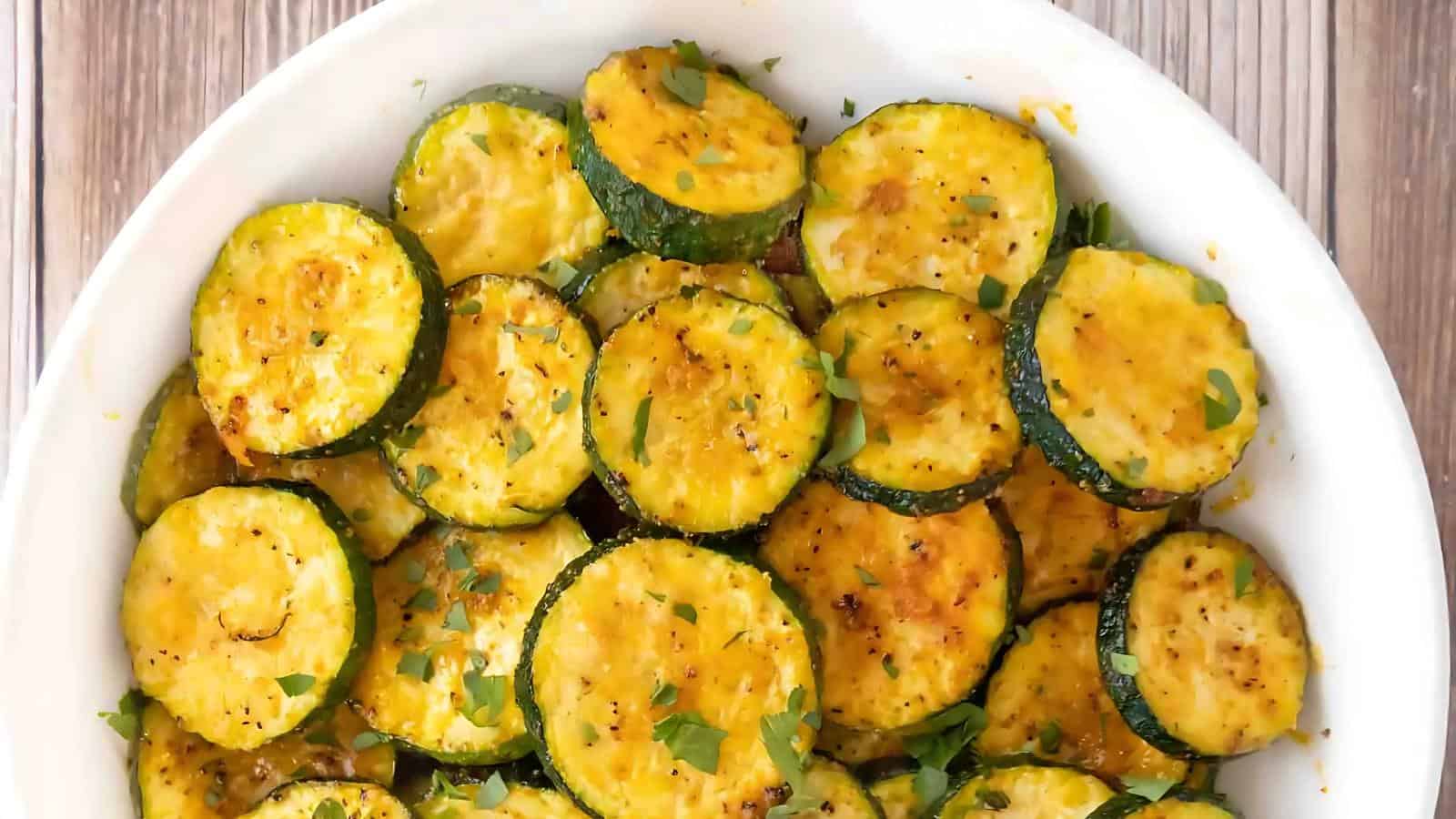 White bowl filled with sliced, seasoned zucchini garnished with herbs on a wooden surface.