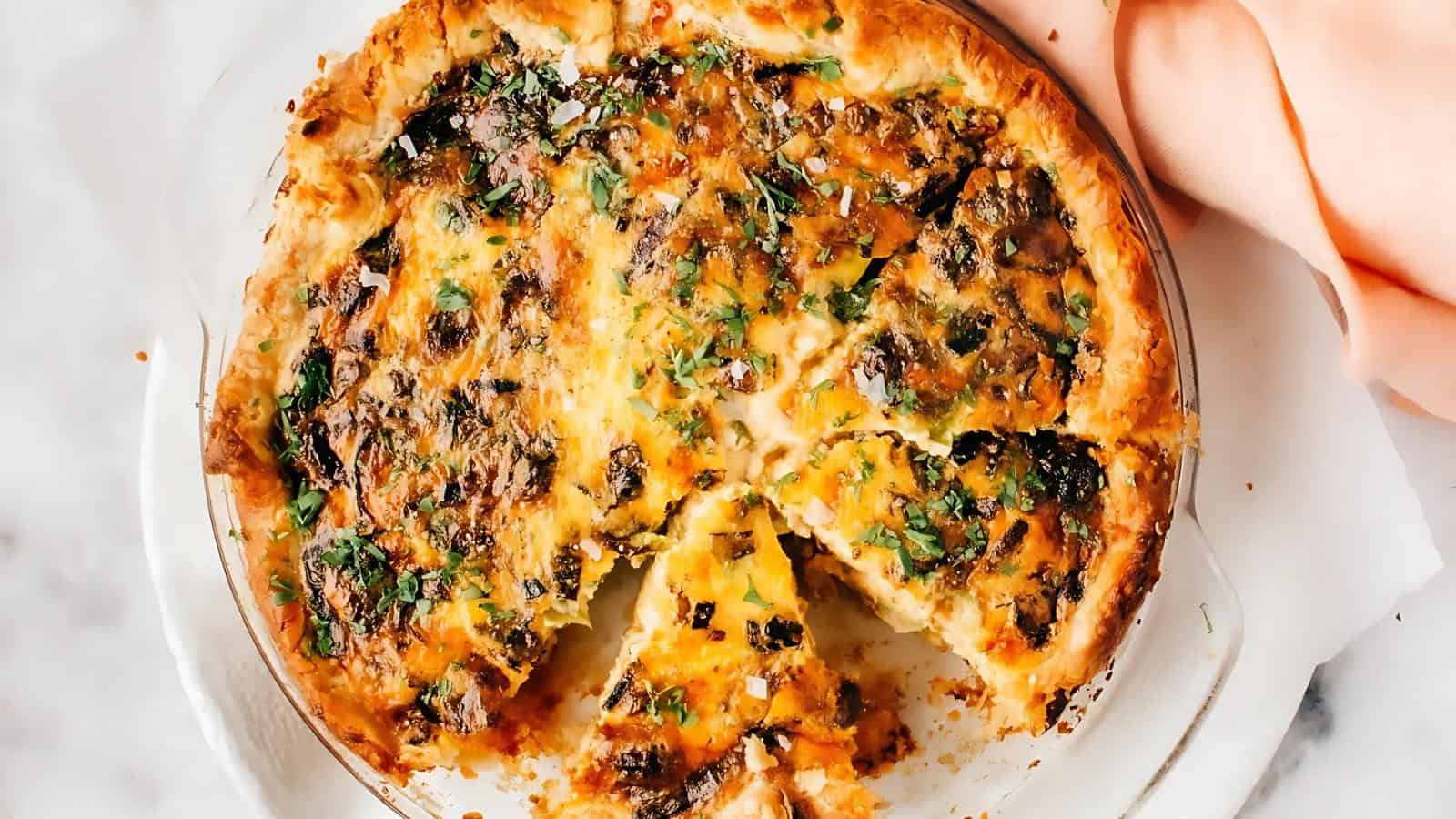A savory pie with a golden crust, filled with cheese, herbs, and mushrooms, partially sliced, on a marble surface.