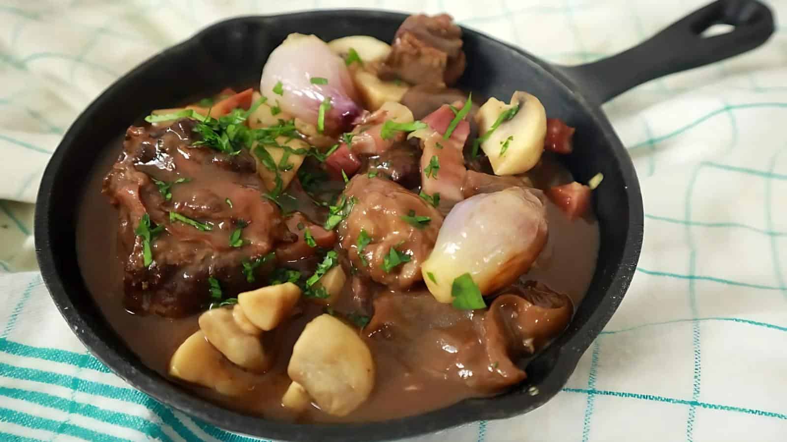 A skillet of beef stew with mushrooms, onions, and herbs in a sauce.