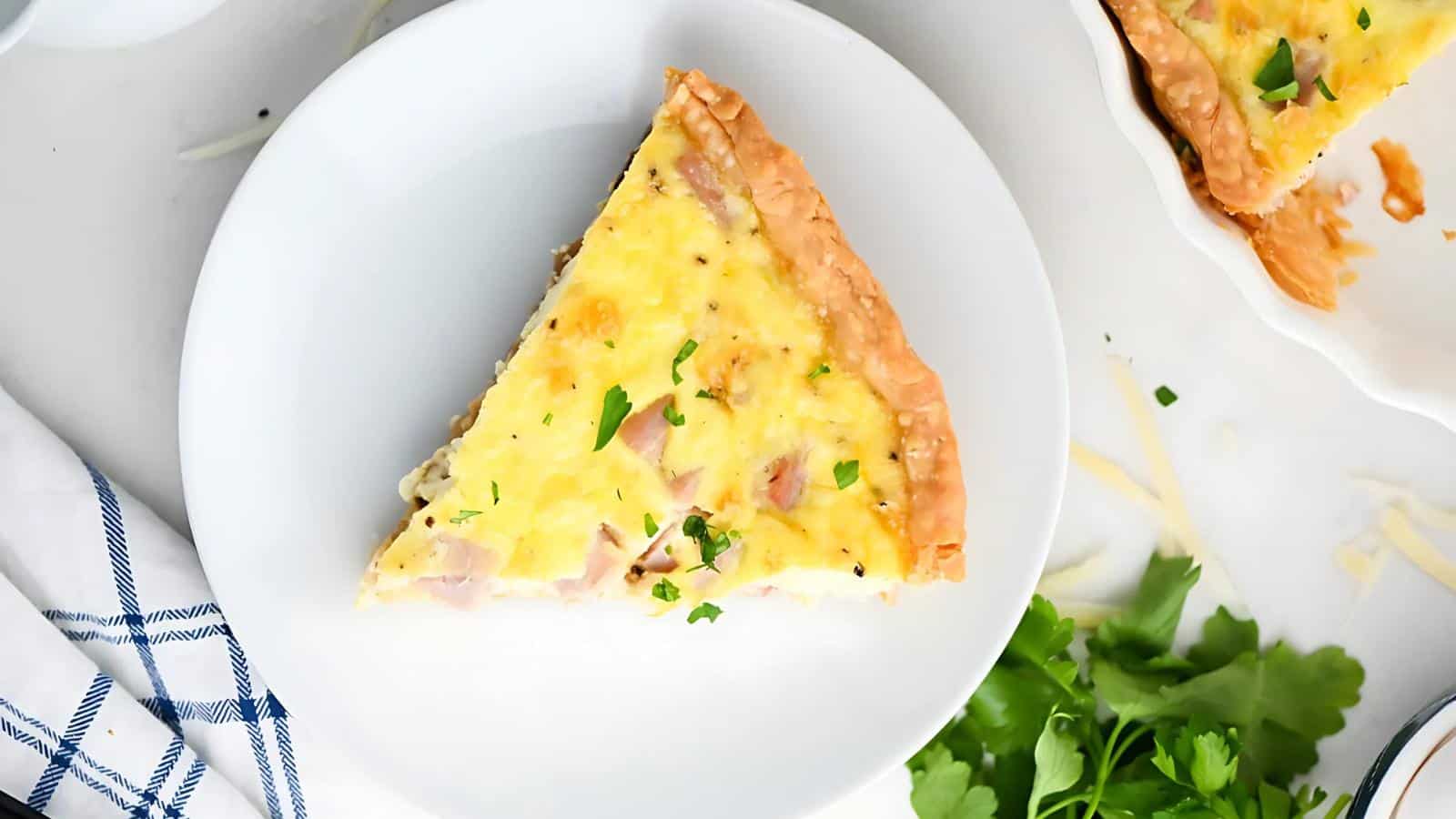 A slice of quiche on a white plate, garnished with herbs.