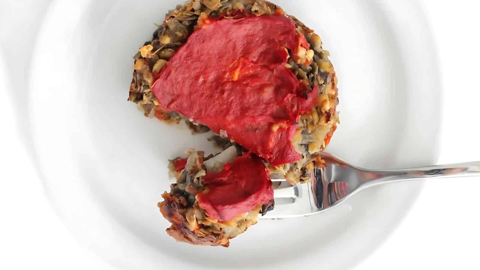 A fork cuts into a lentil loaf topped with tomato glaze on a white plate.