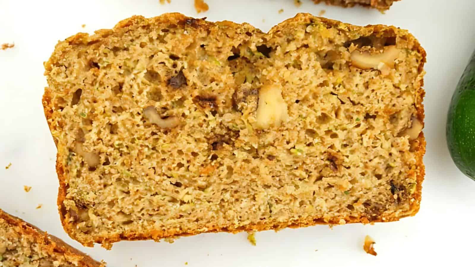 Close-up of a slice of zucchini bread with visible nuts on a white surface.