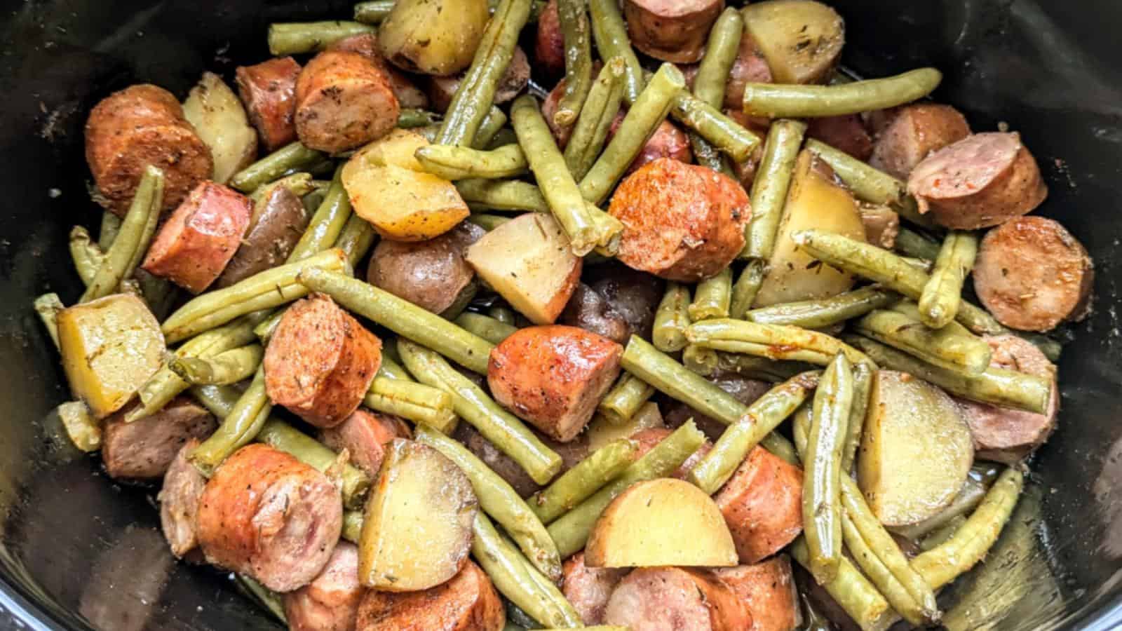 Sliced sausages, green beans, and potato chunks cooked together in a dish.