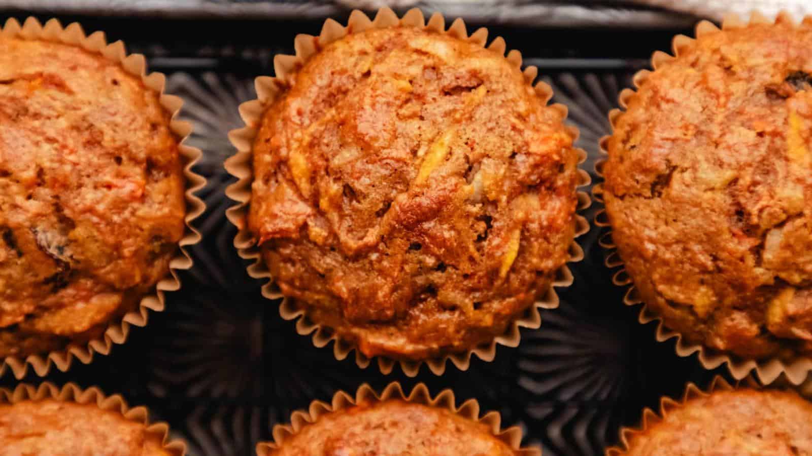 Close-up of six freshly baked muffins in paper liners, placed in rows on a black tray.