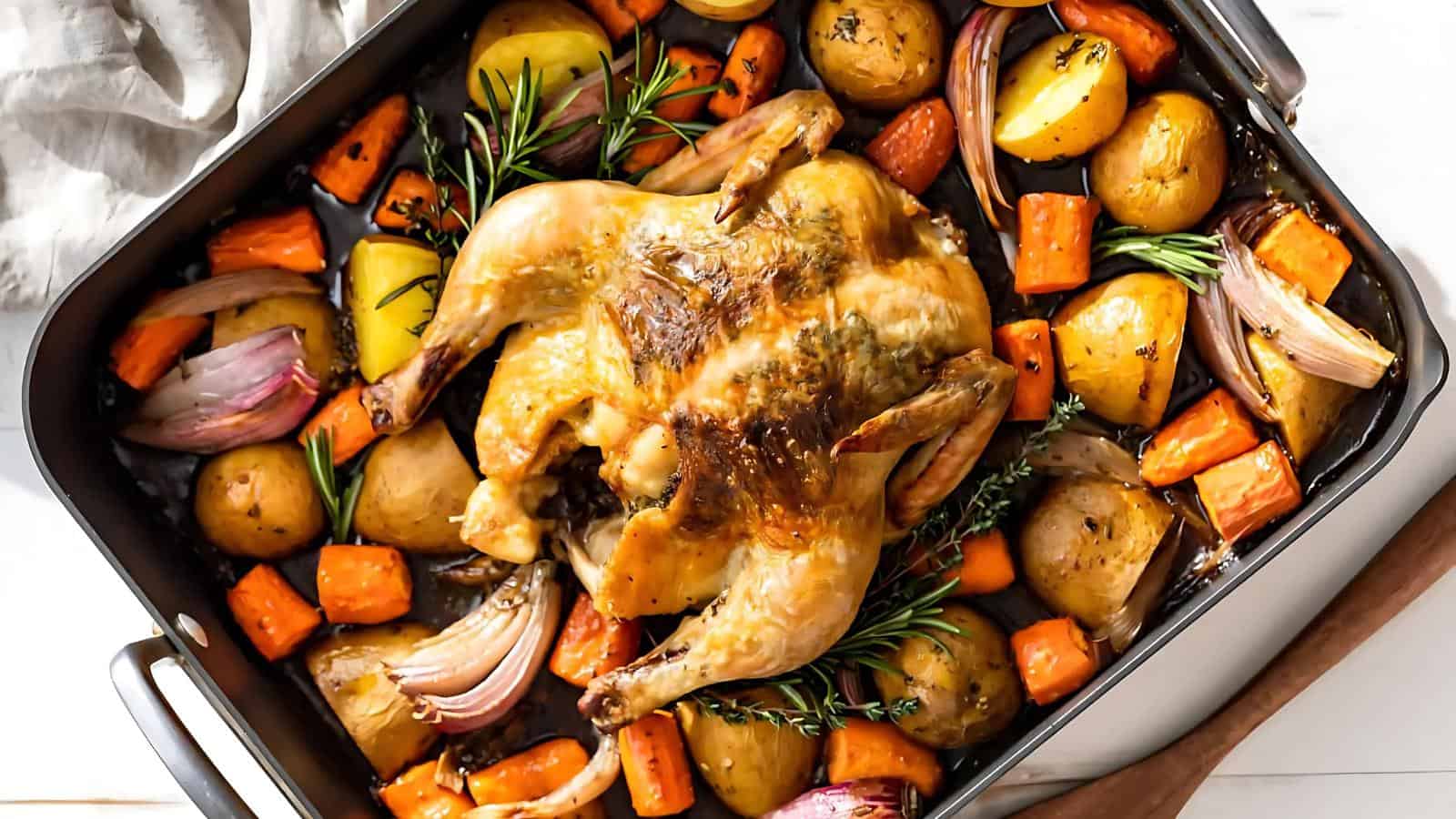 Roasted chicken served in a baking dish with potatoes, carrots, onions, and herbs.