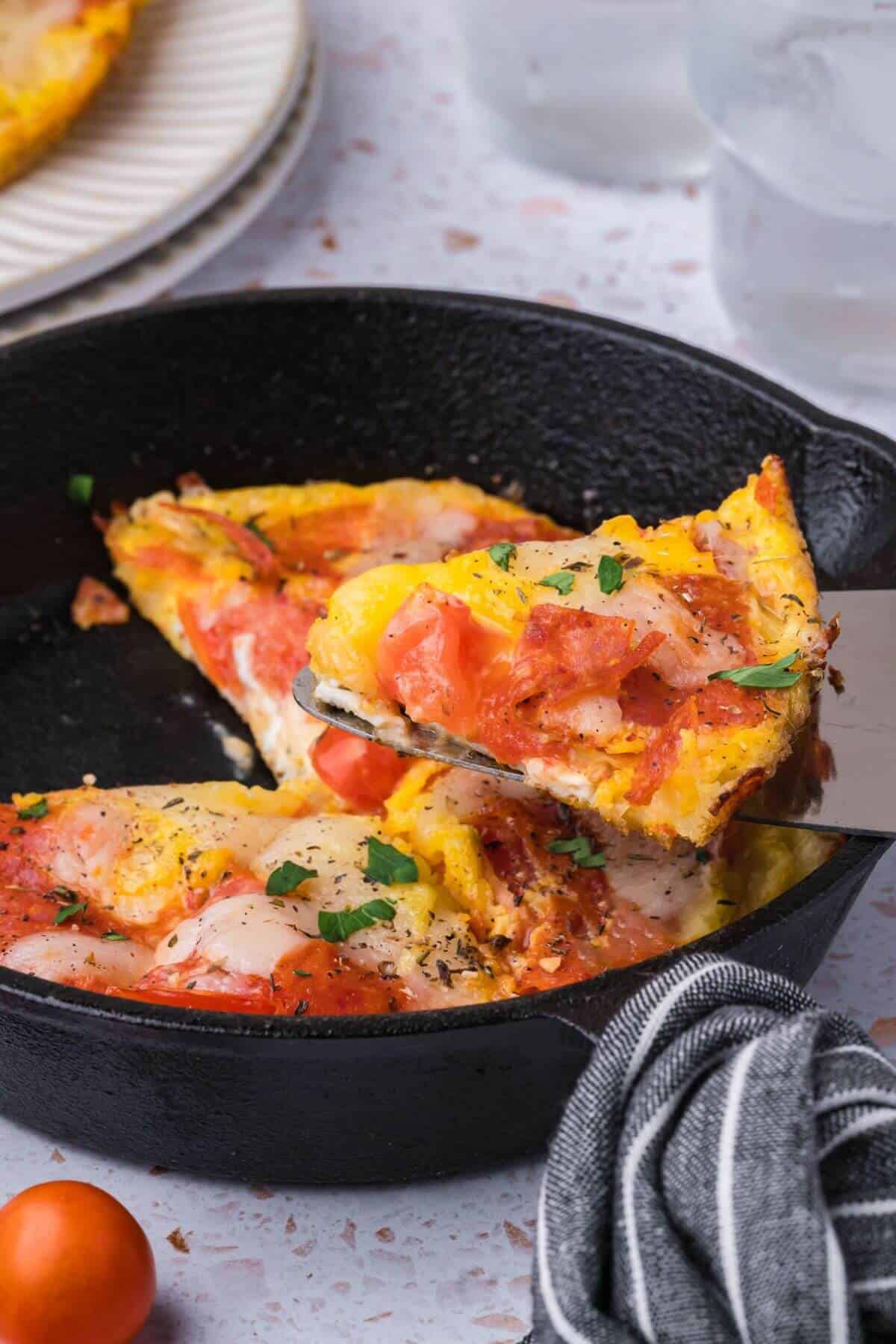 A slice of tomato and cheese pizza is being lifted from a cast iron pan.